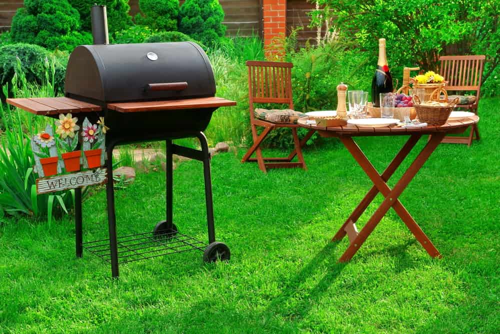 Un outdoor party para dos con un barbecue y una mesita de jardín bellamente servida con detalles para disfrutar el momento.